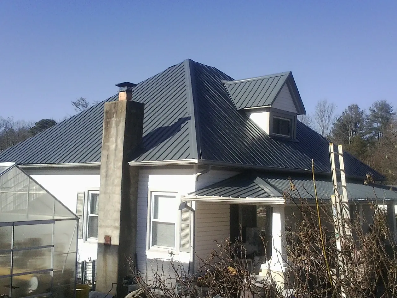 Dark blue standing seam metal roof on a white farmhouse with dormer — Slate & Tile Roof Repair by Roofing Brothers in Winston
