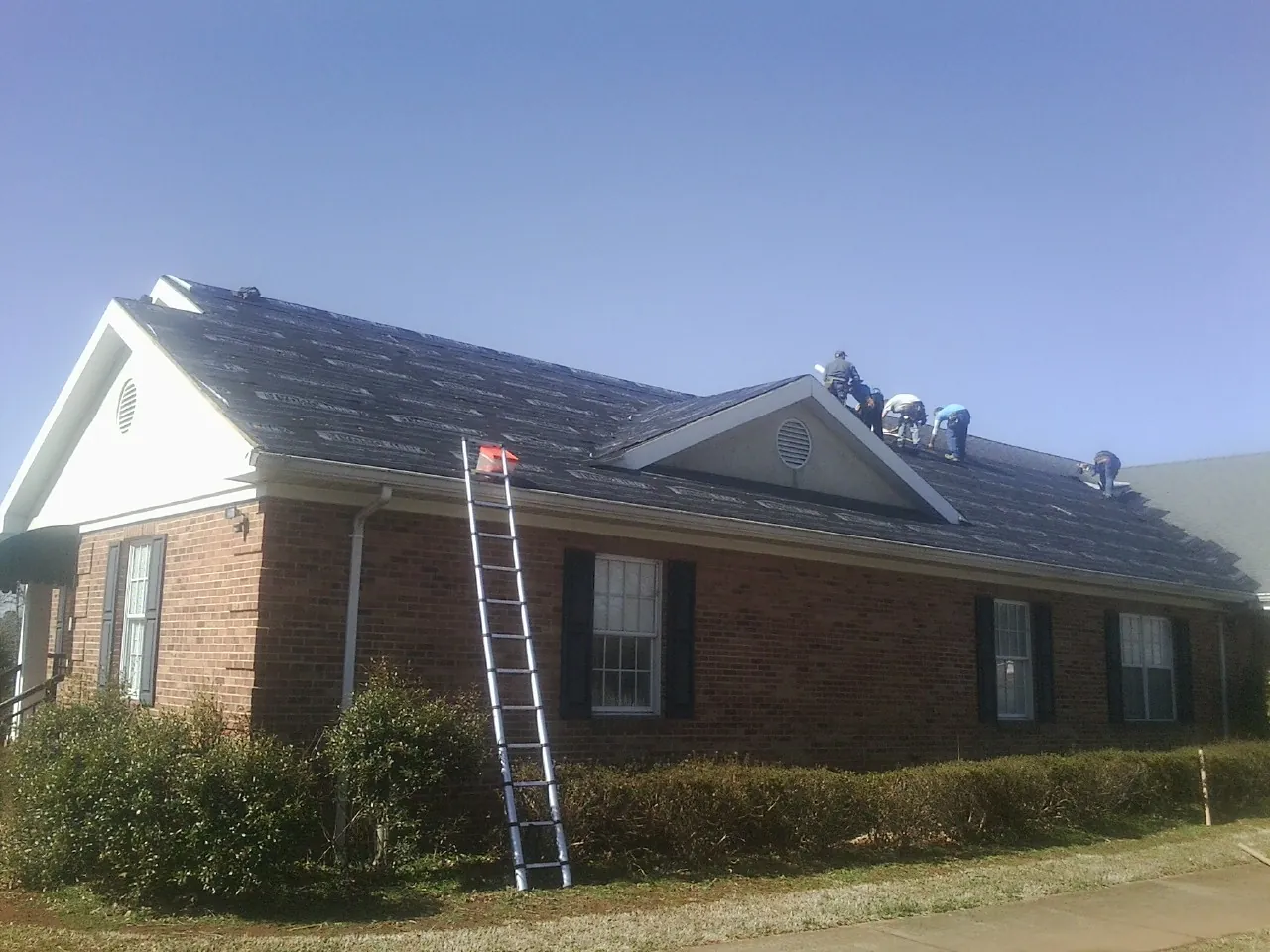 Crew tearing shingles off a brick ranch roof with a ladder set — Metal Roof Repair work by our crew in Winston