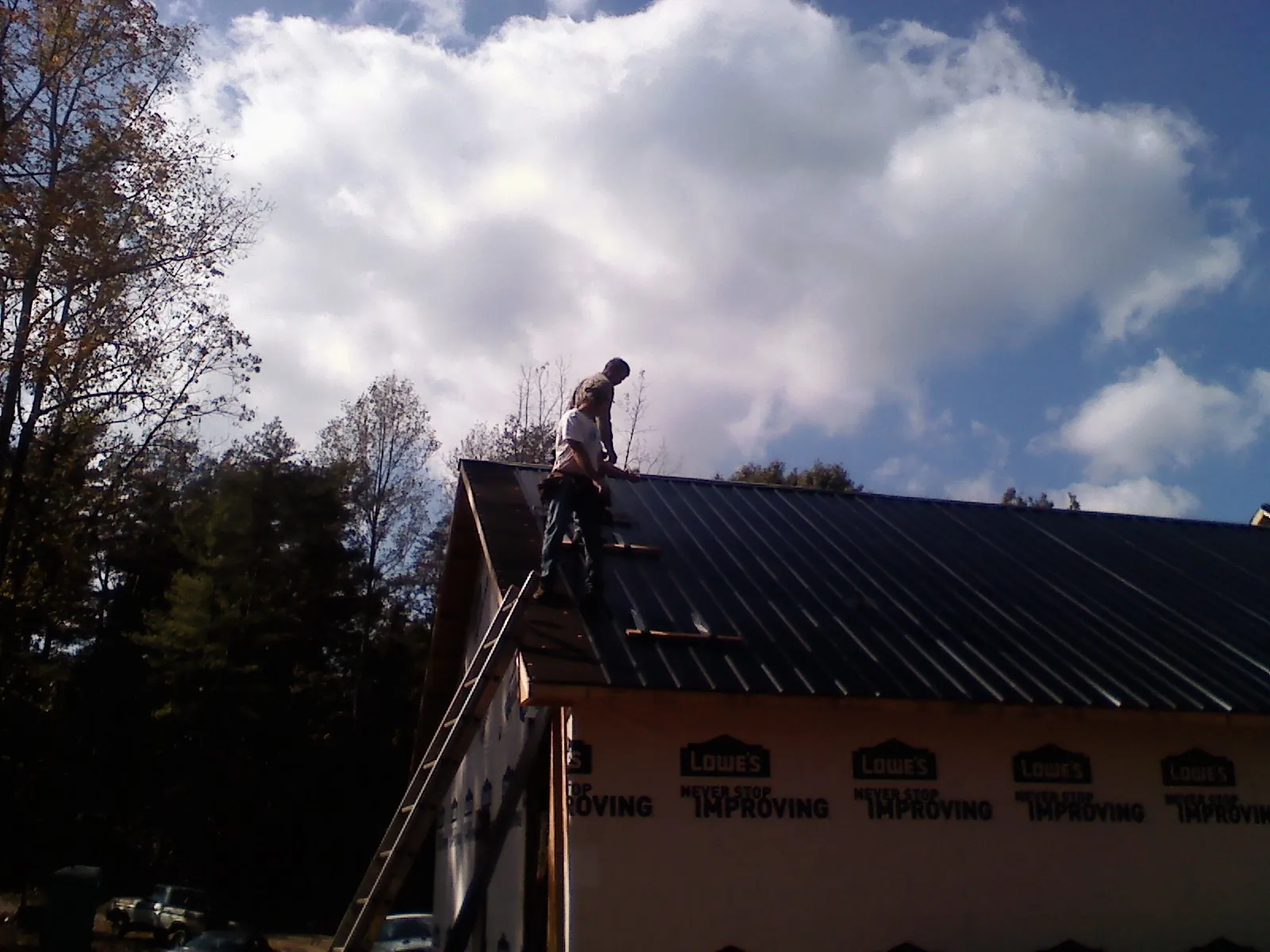 Roofer fastening dark metal panels high against a cloudy sky, from a Roof Inspection job in Winston