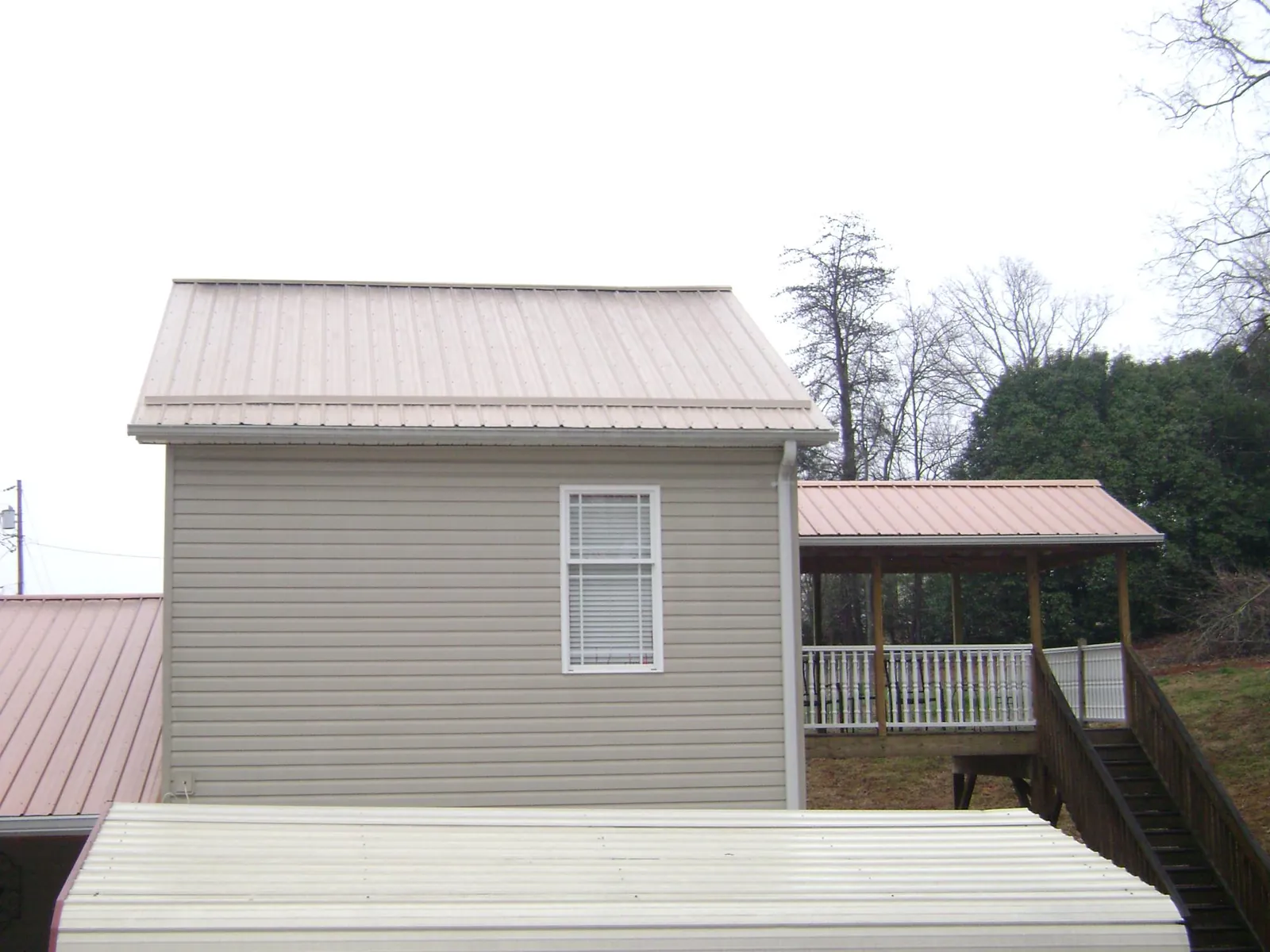 Tan metal roofs on a two story addition and attached porch, from a Roof Replacement job in Winston